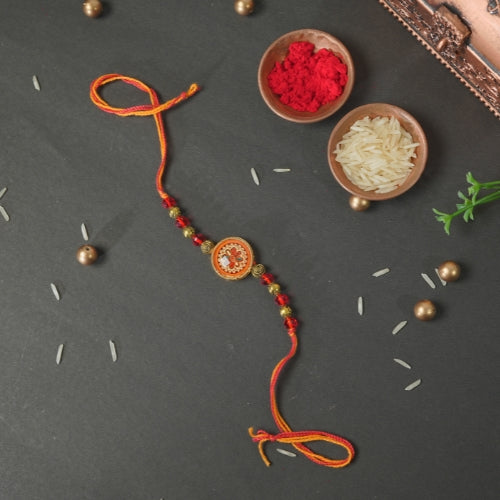 Handmade Rakhi – Traditional Orange Thread Rakhi with Circular Beaded Centerpiece